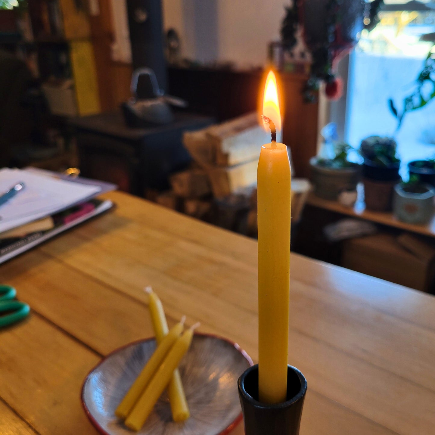 Tall beeswax mini-taper burns in a taper holder while unlit candles lie on a mushroom plate in the background.