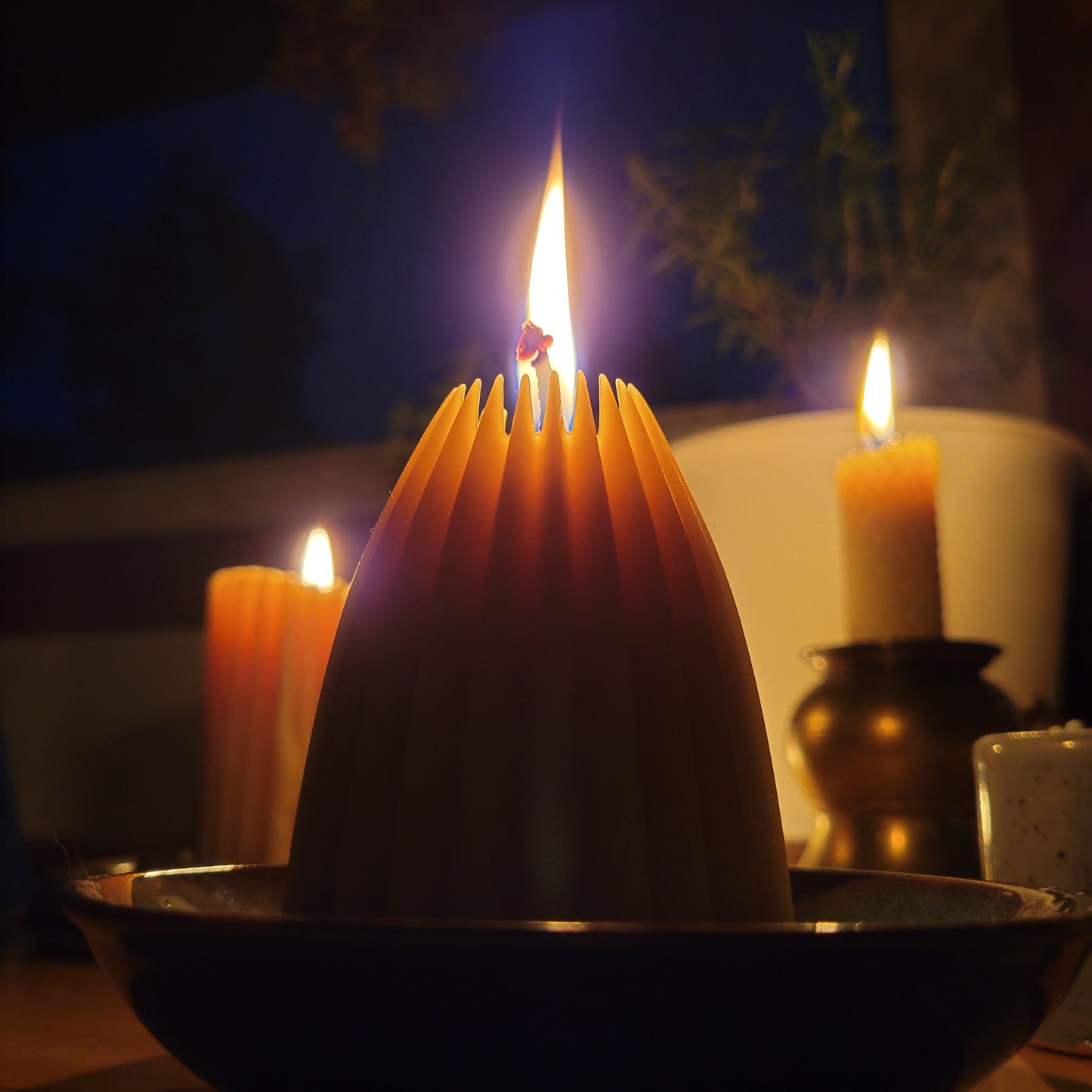 Fluted pyramid candle lit with two candles in background