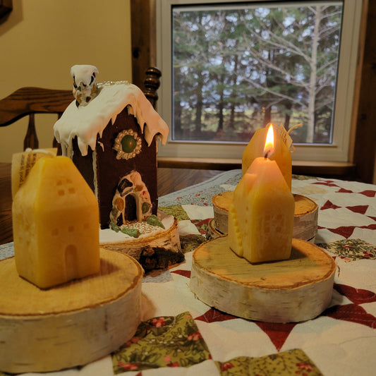Plain beeswax little house candles with a mini gingerbread house in the background.
