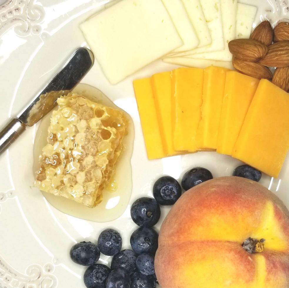 Square of honeycomb on charcuterie board with cheeses, nuts, crackers, blueberries and fresh peach