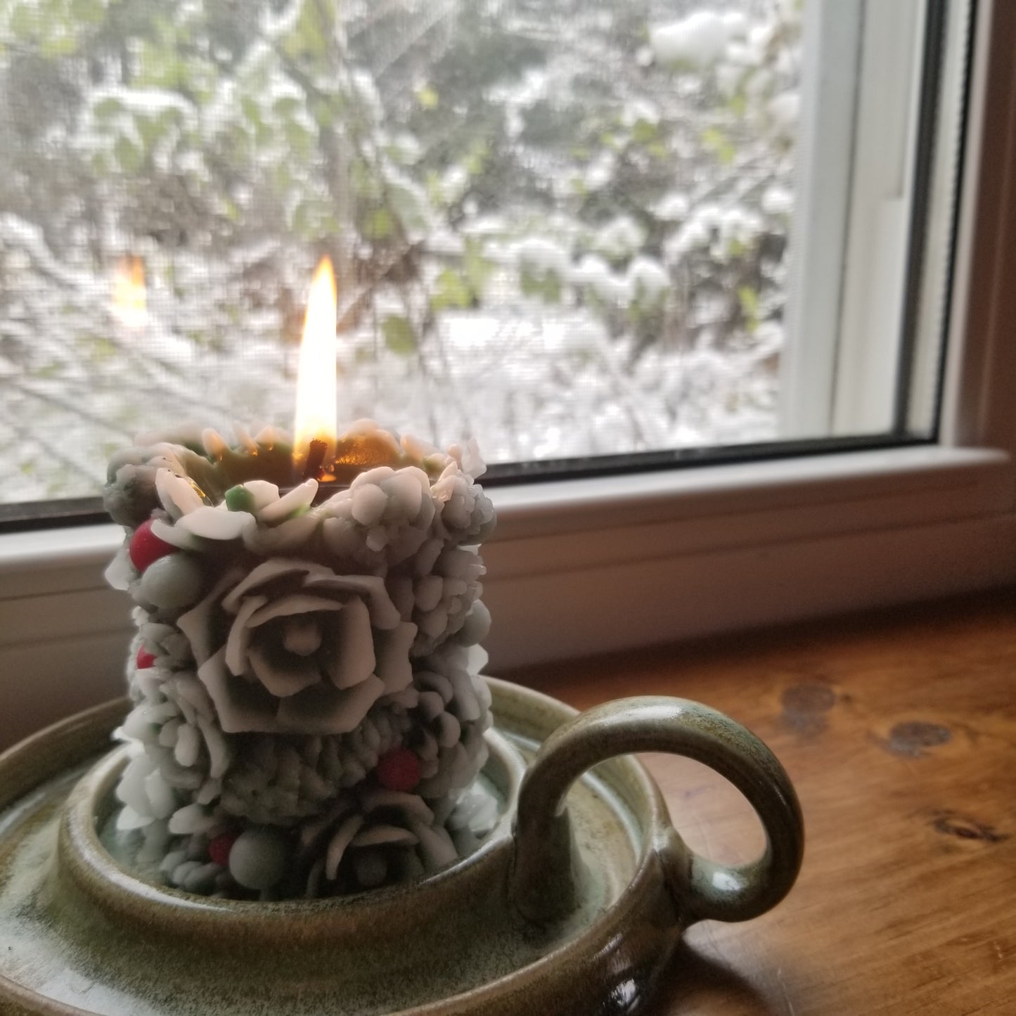 Beeswax greenery pillar with lit flame sitting in a window