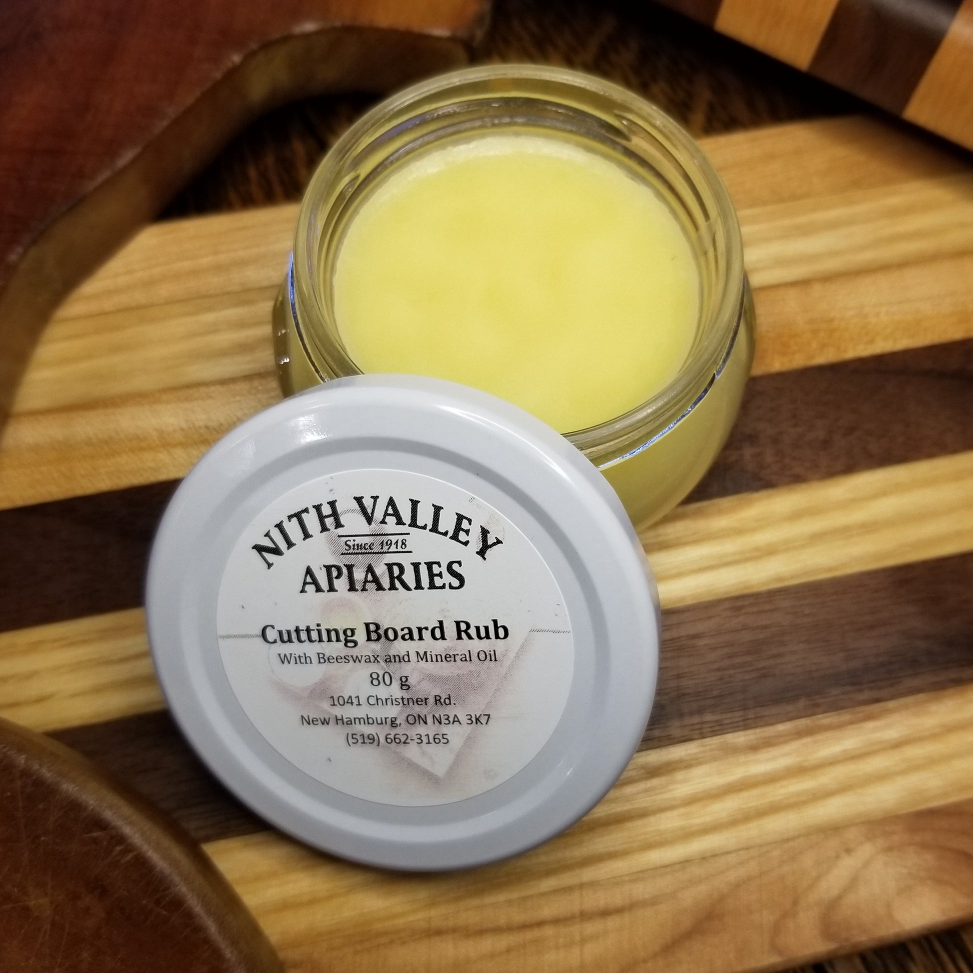 Jar of cutting board rub sits with lid off on top of a kitchen cutting board.