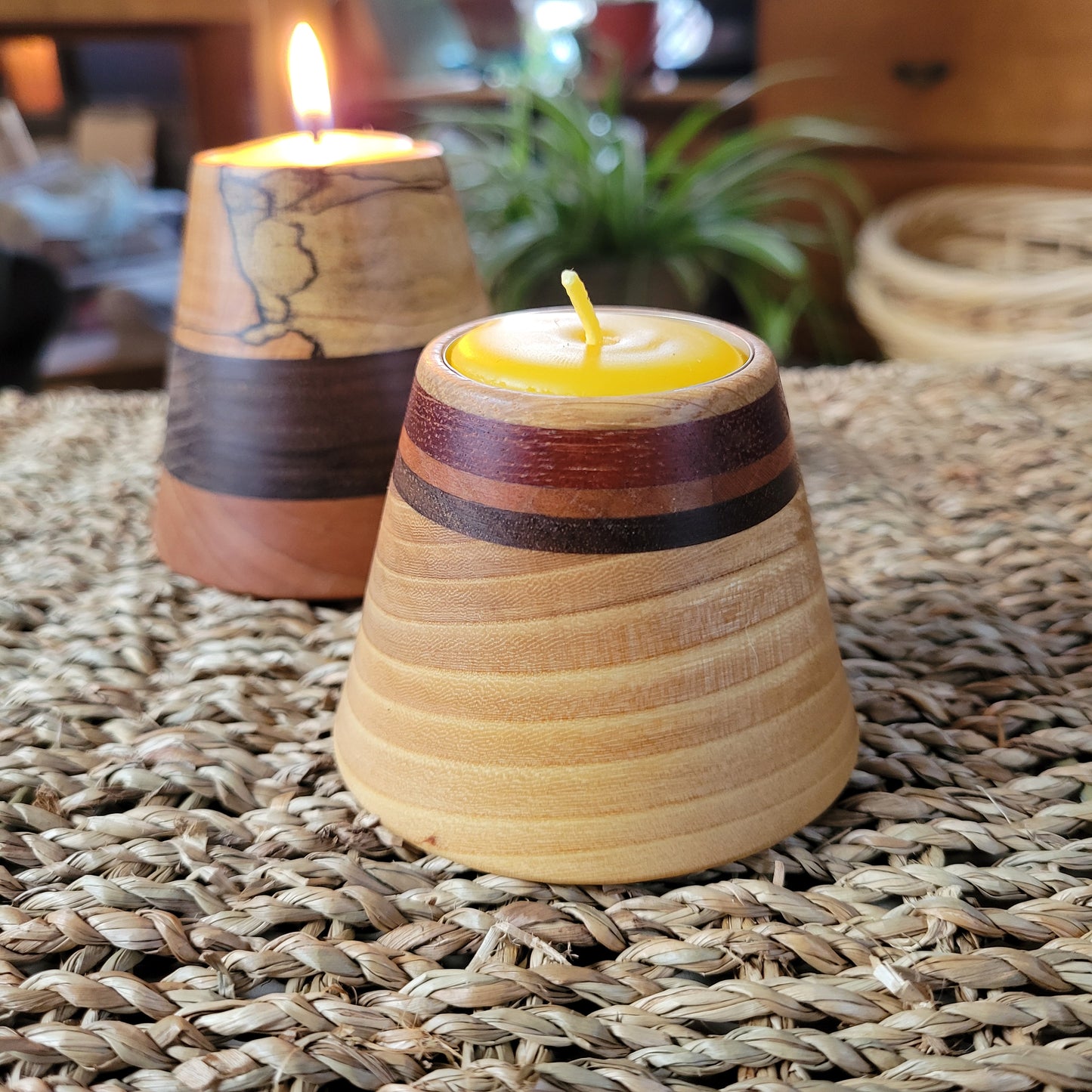 turned wooden tealight holder sits on a wicker table with plant in background