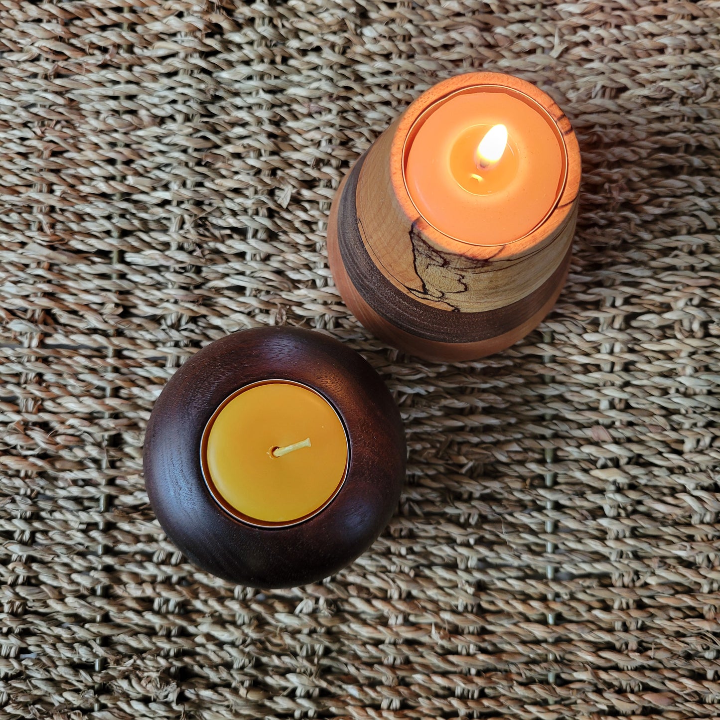 Two candles in wooden holders on a textured woven surface