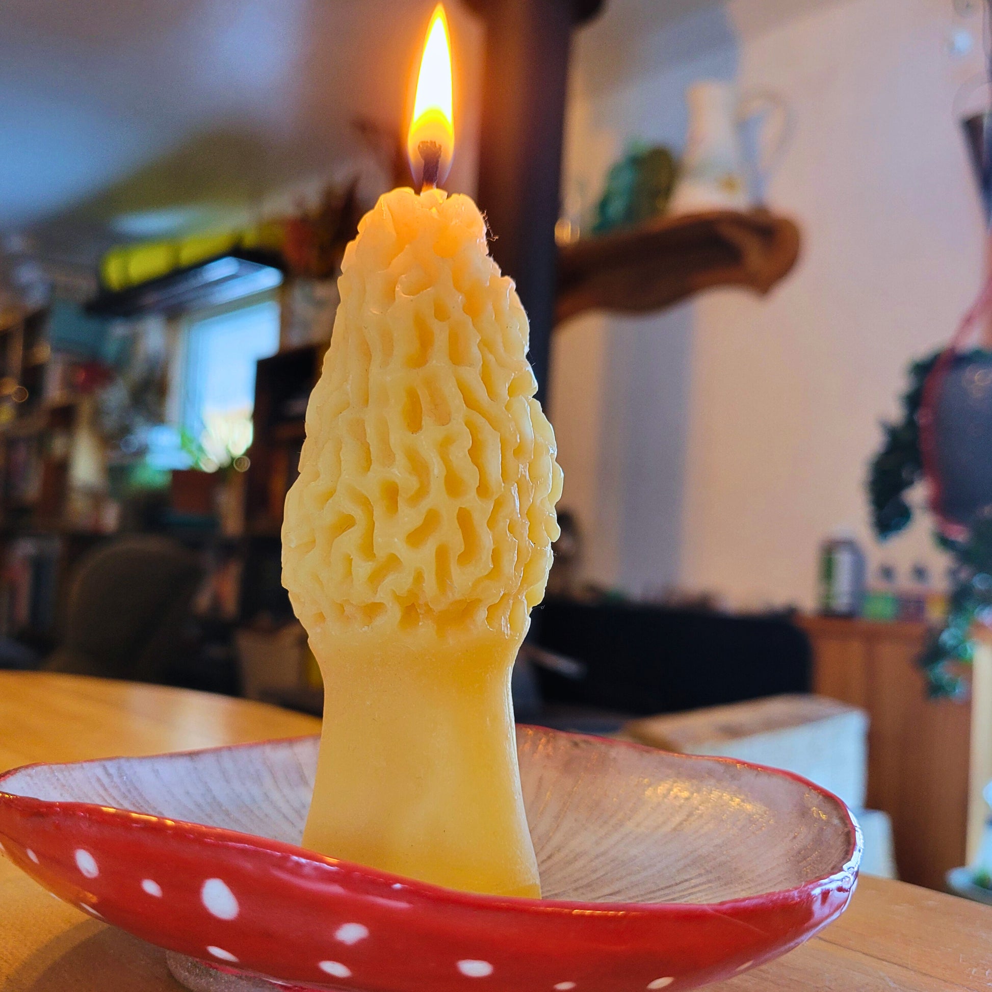 Beeswax morel mushroom candle burns on a plate shaped like a mushroom cap.