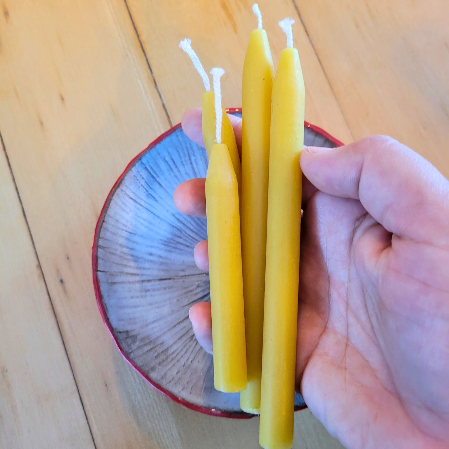 hand holds beeswax mini tapers in both short and tall sizes. Mushroom plate in background.