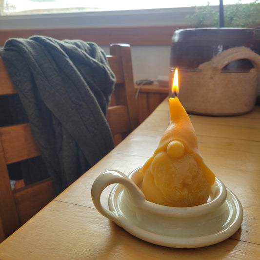 Grimble Grumble beeswax gnome candle lit in a white pillar candle plate