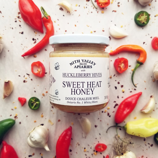 Sweet Heat Honey 300g Jar with garlic, hot peppers and pepper flakes artfully arranged in the background.