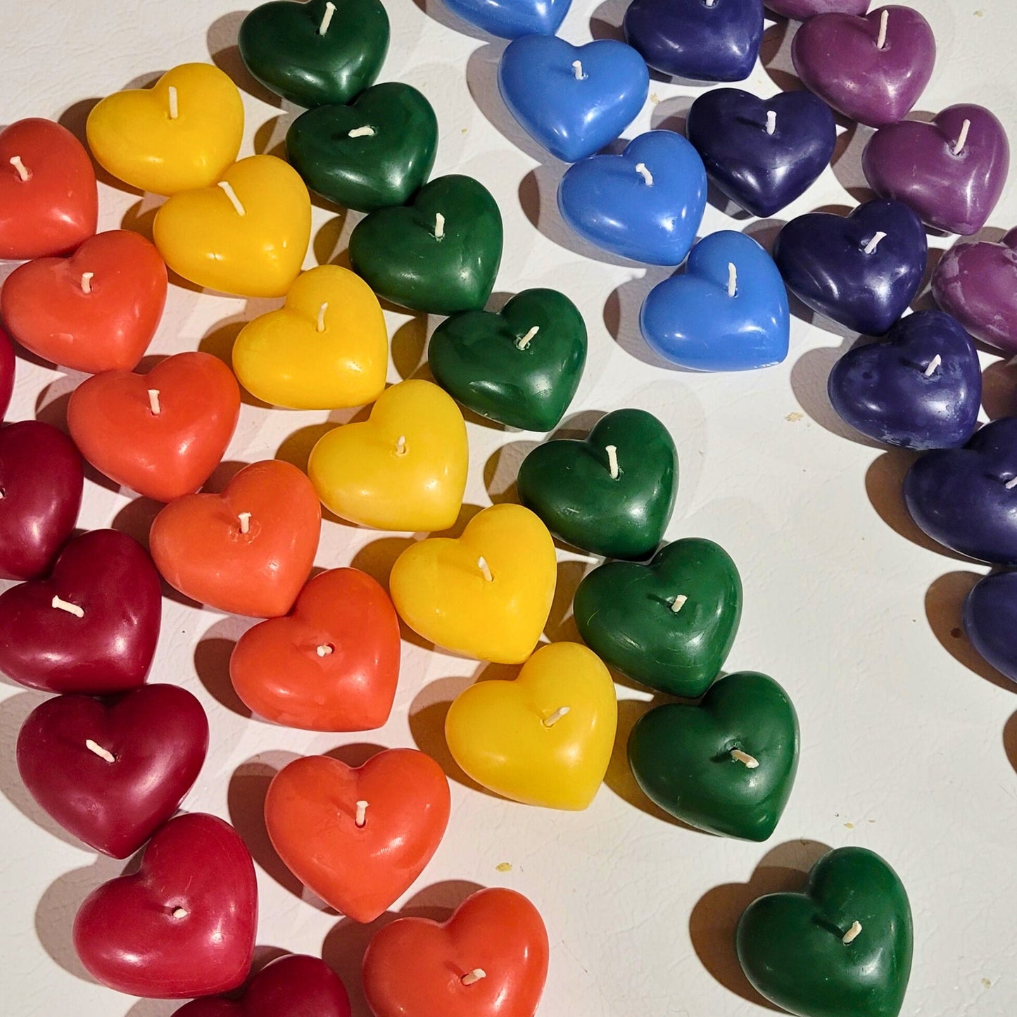 Heart-shaped candles in various colors arranged on a white surface