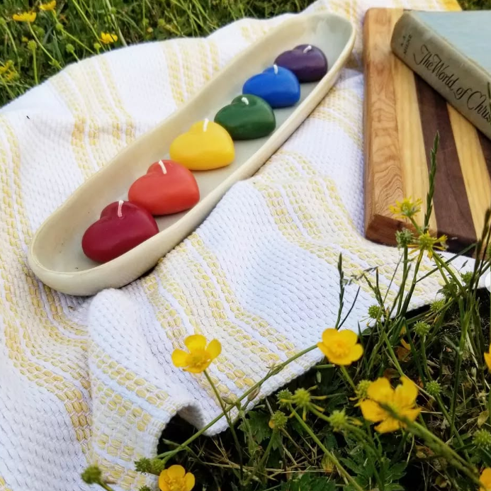 Colorful heart-shaped candles in a tray on a white blanket with yellow flowers and a book.