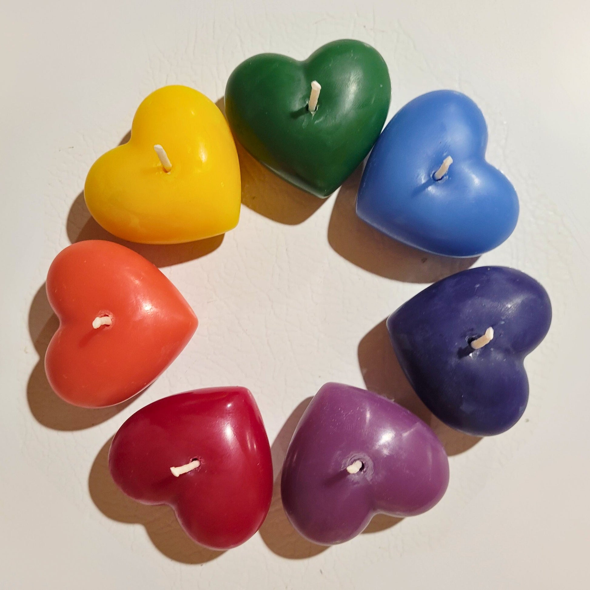 Heart-shaped candles in rainbow colors arranged in a circle on a white background