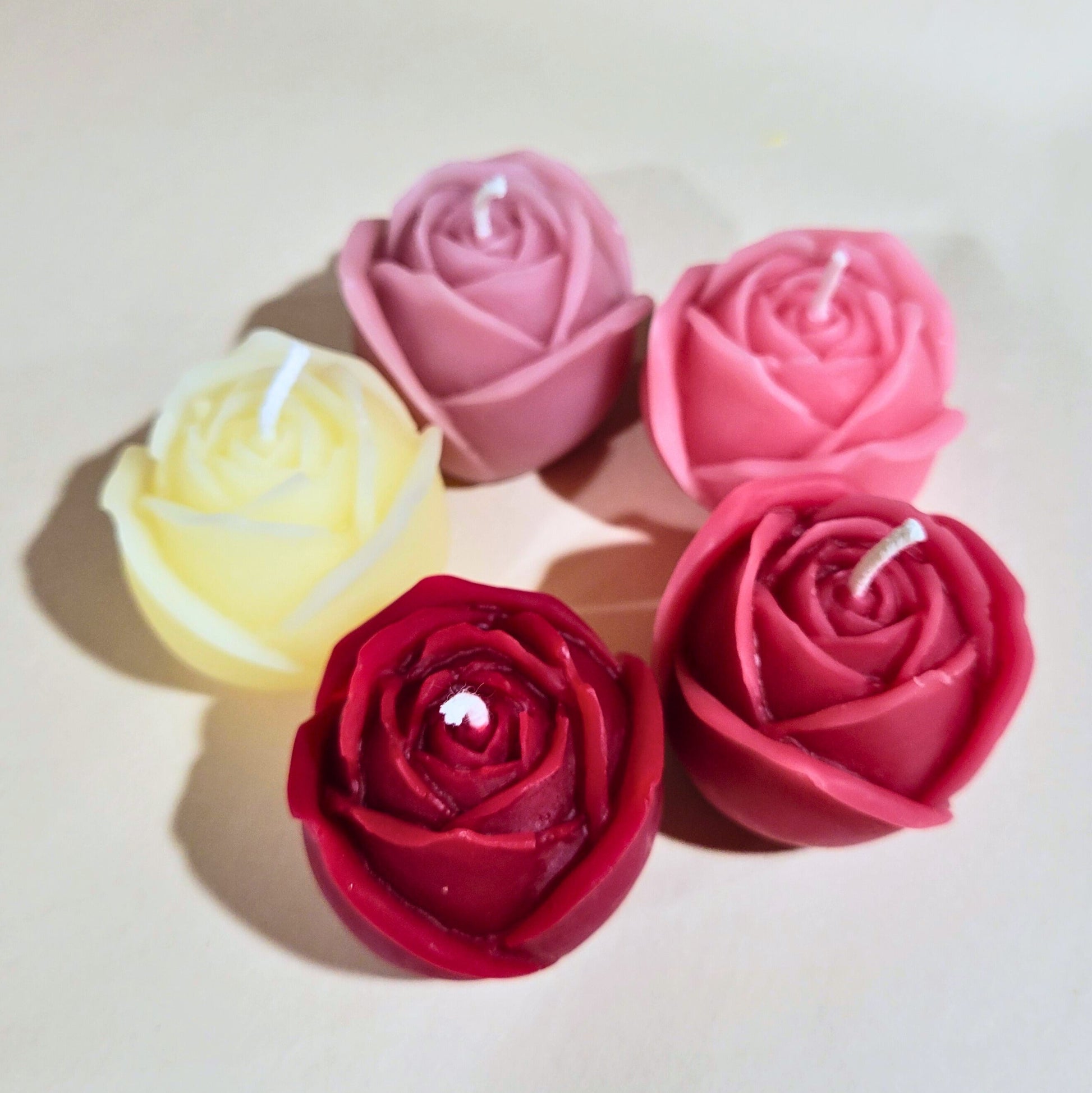 Five rose-shaped candles in white, shades of pink and ruby red on a light background