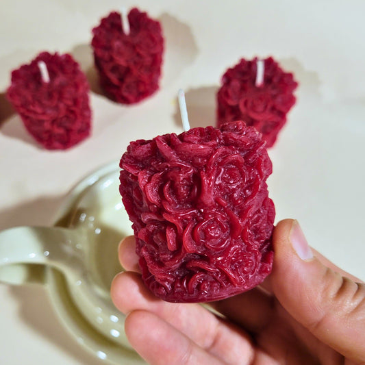 Red rose-textured votive candle held by a hand with more candles in the background.