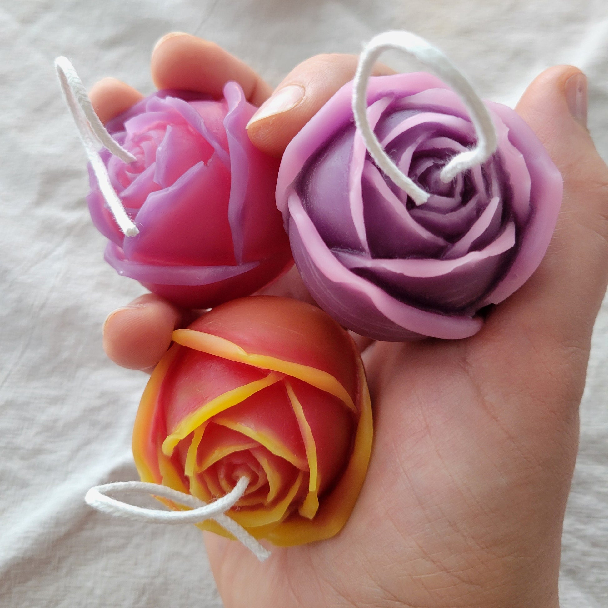 Three colorful rose-shaped candles held in a hand against a white background