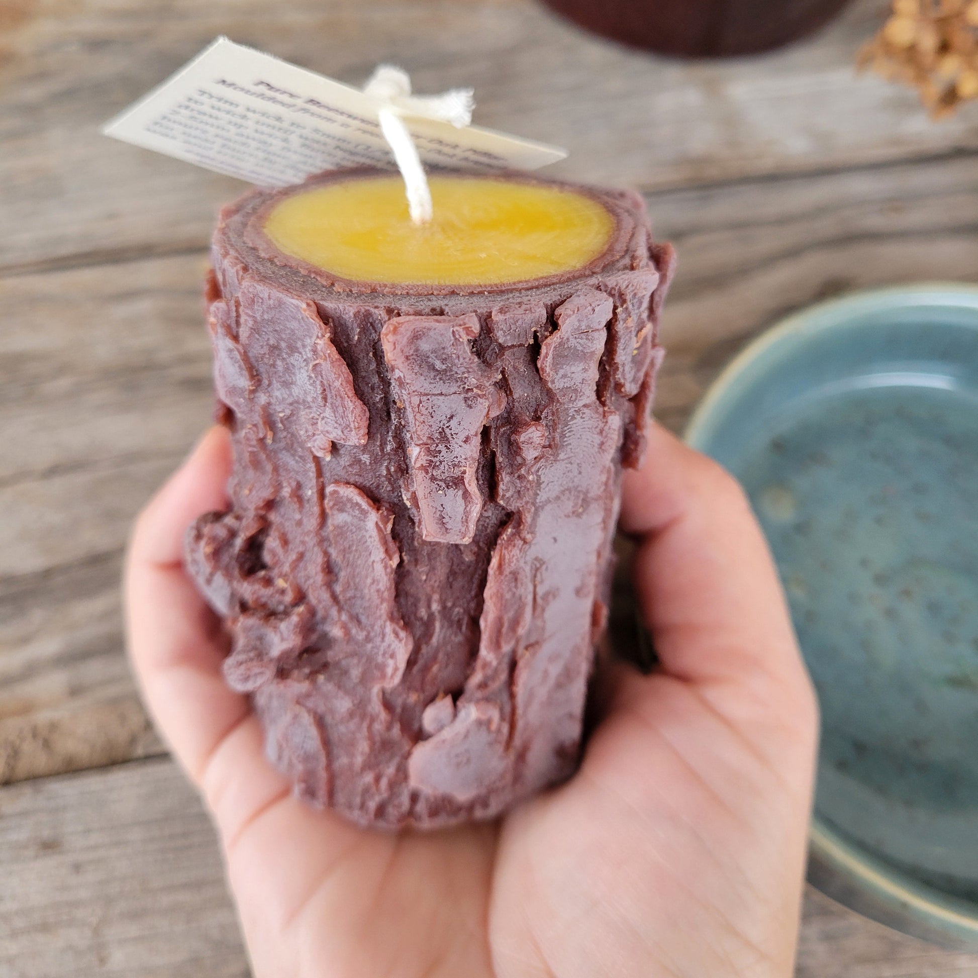 Hand holding a rustic log-shaped candle with a wooden background