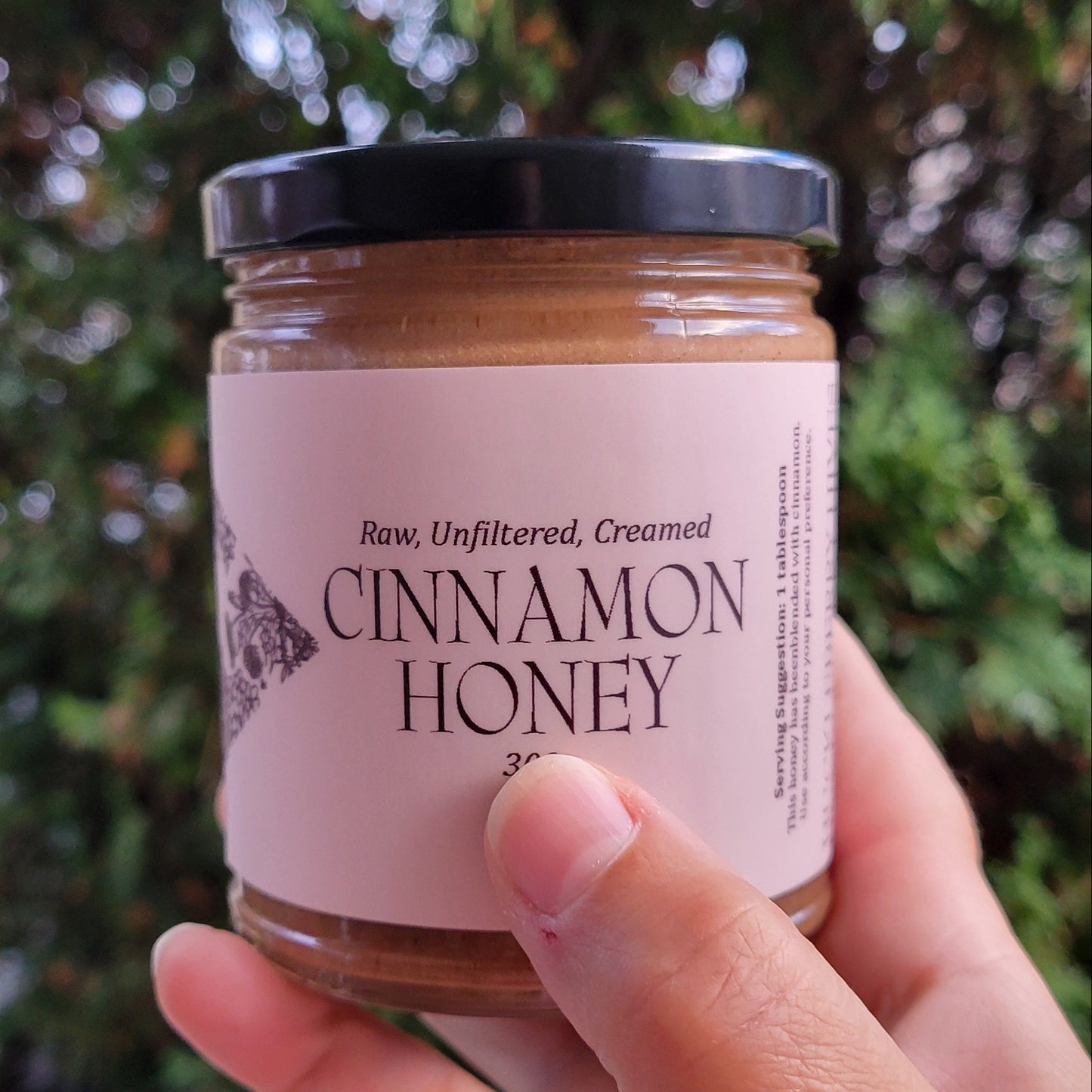 Hand holding a jar of cinnamon honey with a blurred natural background