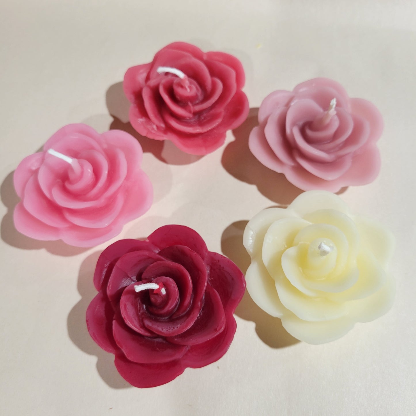 Set of five rose-shaped candles in shades of pink, red, and white on a light background