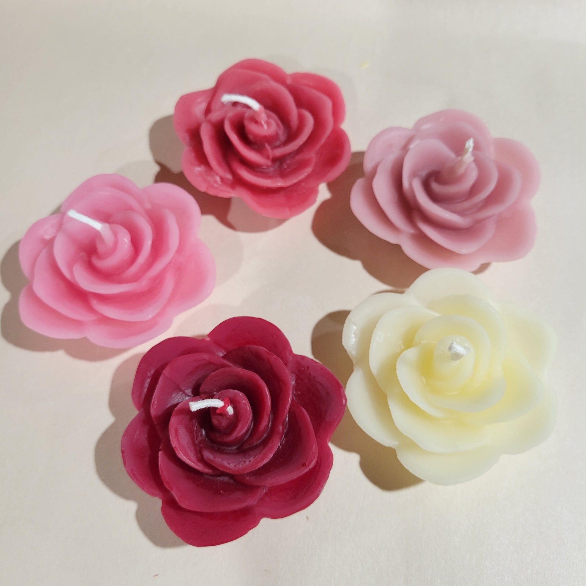 Set of five rose-shaped candles in shades of pink, red, and white on a light background