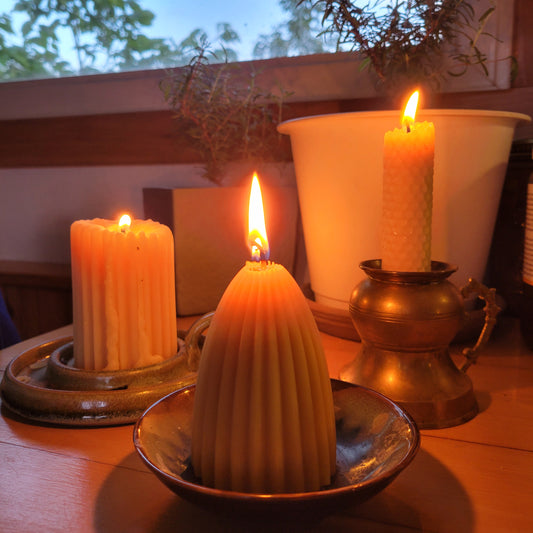 fluted pyamid candle, just lit with 2 candles and plants in the background