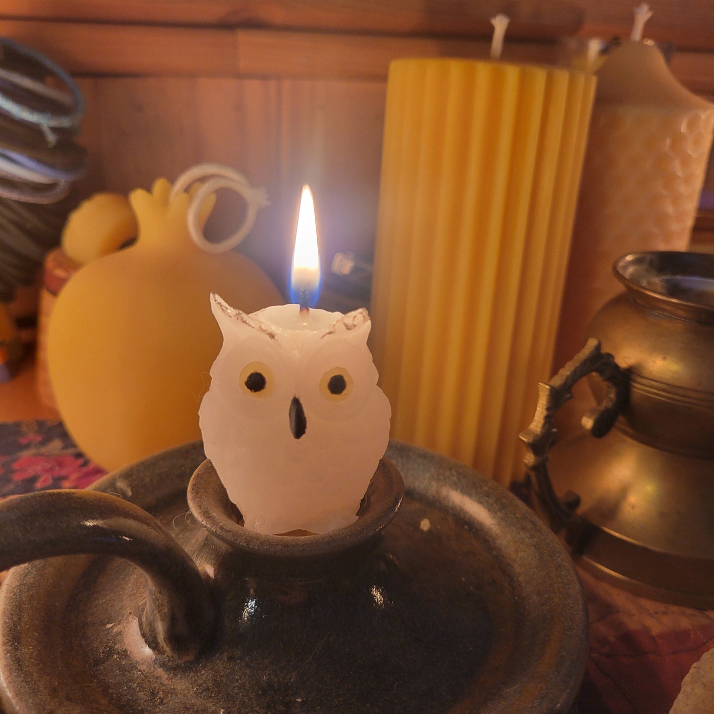 white charcoal filtered beeswax owl candle with yellow eyes and a black beak in a taper holder, with un-lit candles in the background