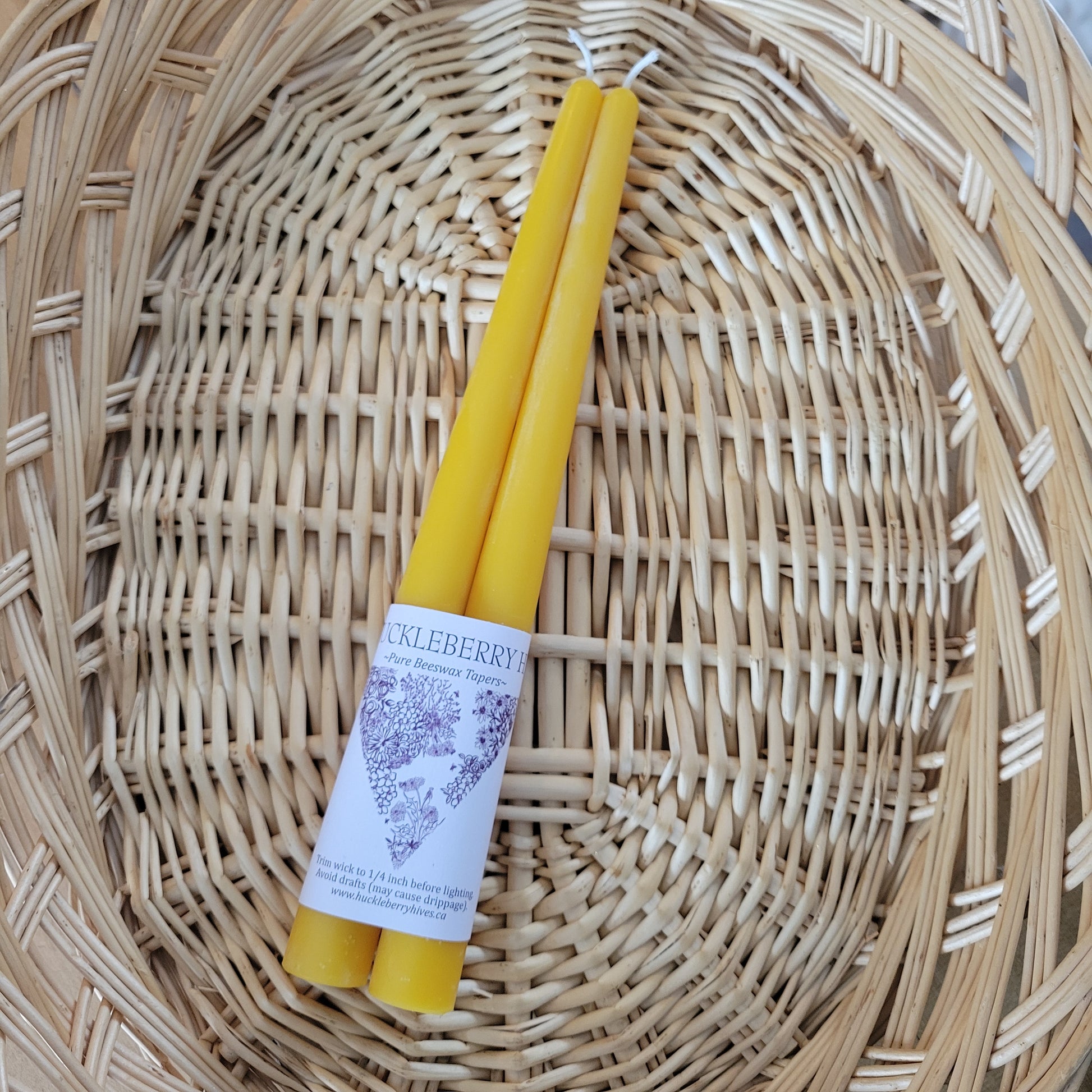 Two yellow beeswax taper candles with a label on a wicker surface