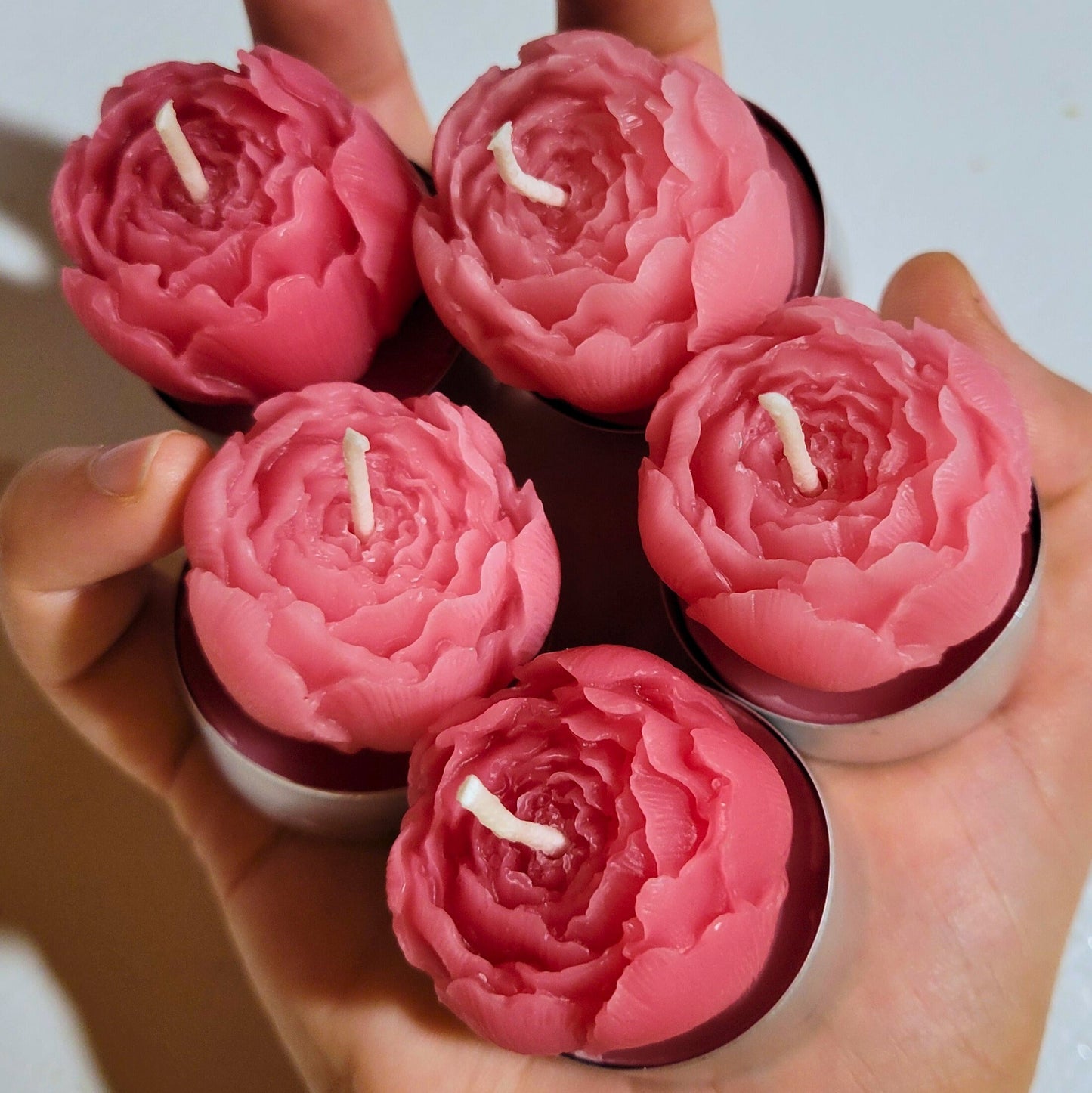 Five pink peony shaped candles held in a hand against a light background