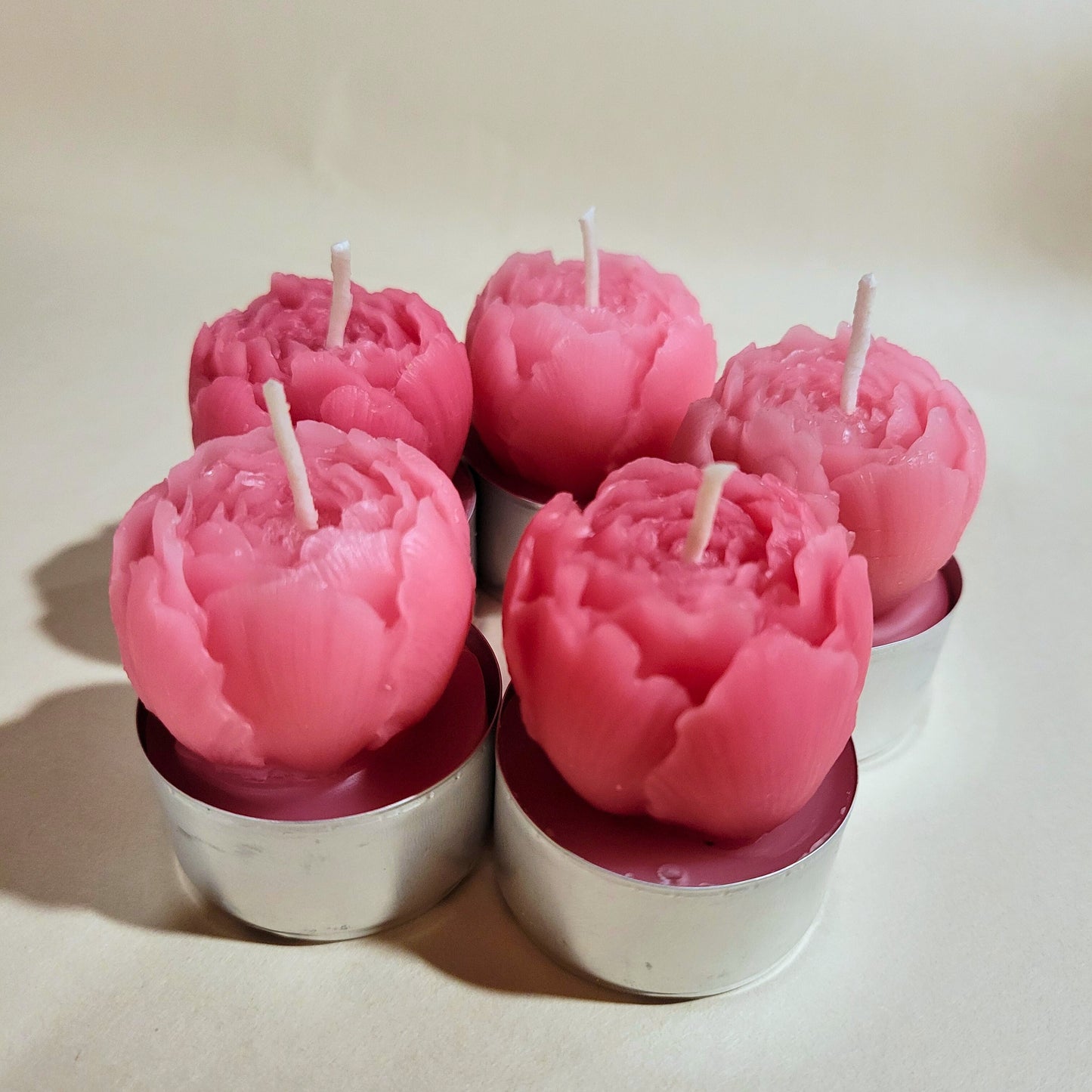 Pink flower-shaped candles in tin holders on a beige background