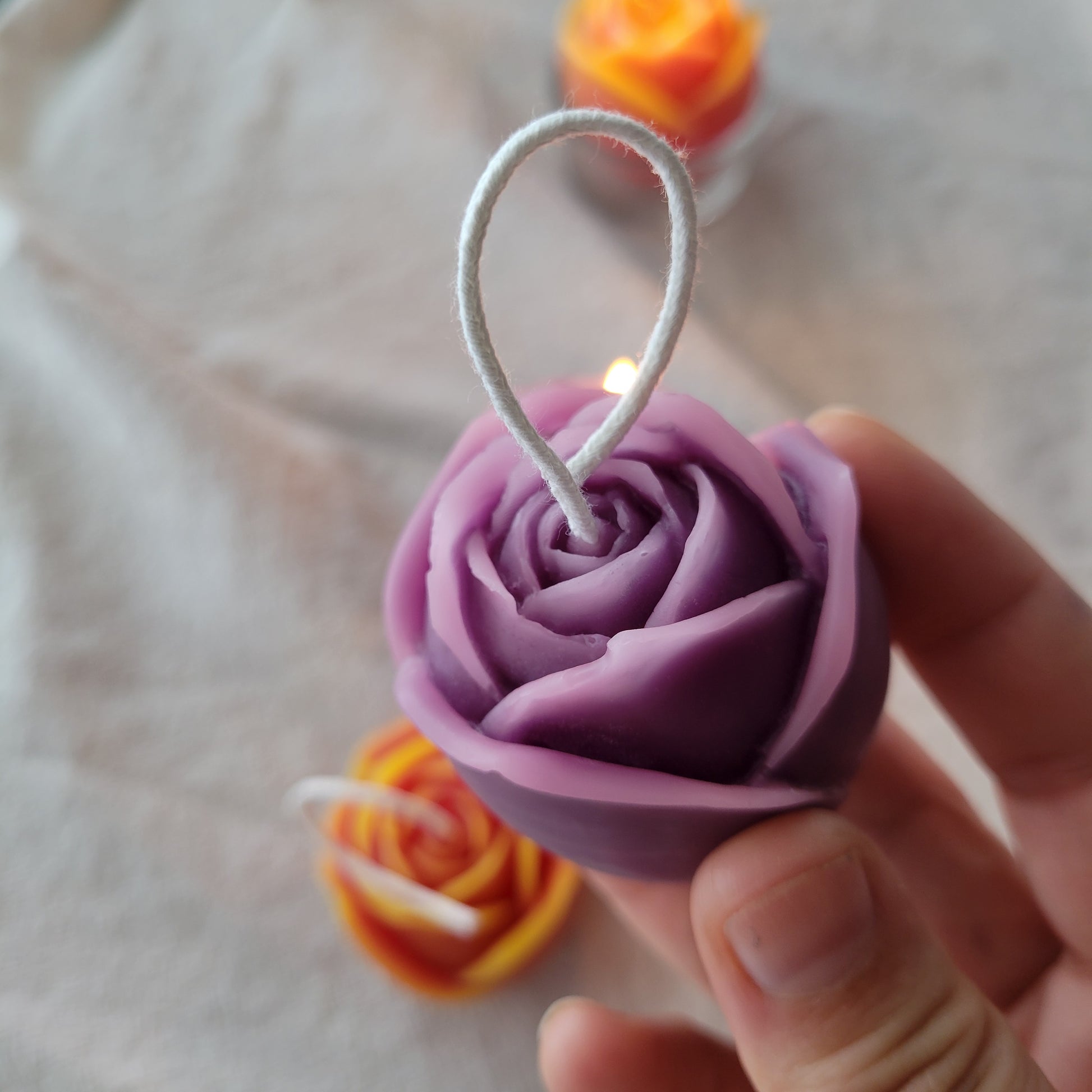 pink and purple candle held by a hand with a blurred white background