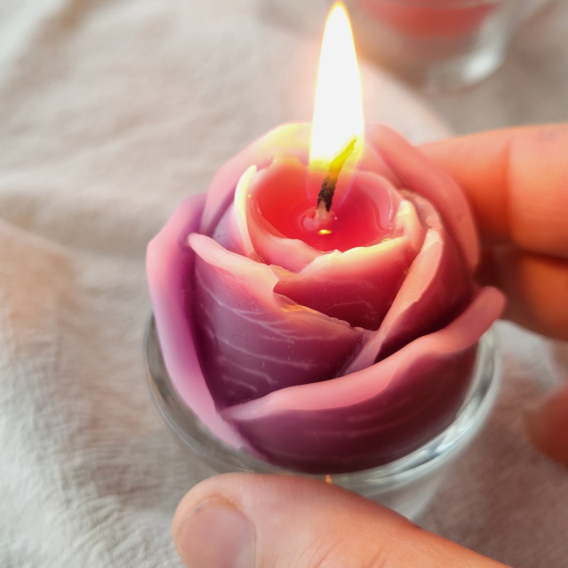 Rose-shaped candle with a lit wick held by a hand on a light background