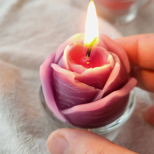 Rose-shaped candle with a lit wick held by a hand on a light background