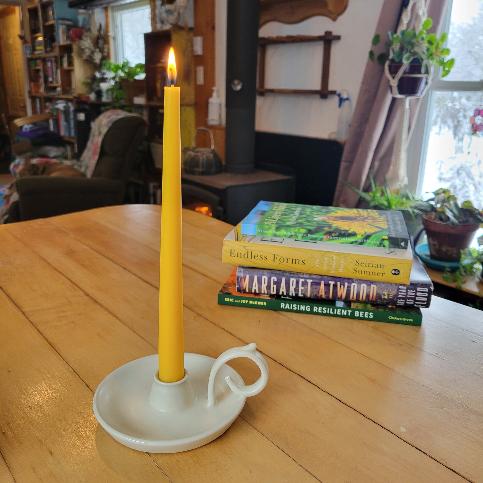 white taper candle holder sits on table with lit taper and a stack of books sits in the background