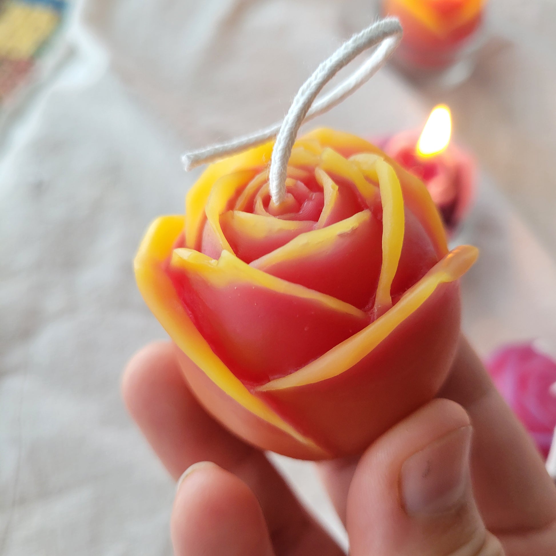  yellow and pink rose-shaped candle held by a hand against a blurred background