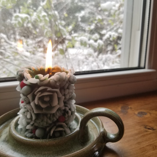 Beeswax greenery pillar with lit flame sitting in a window