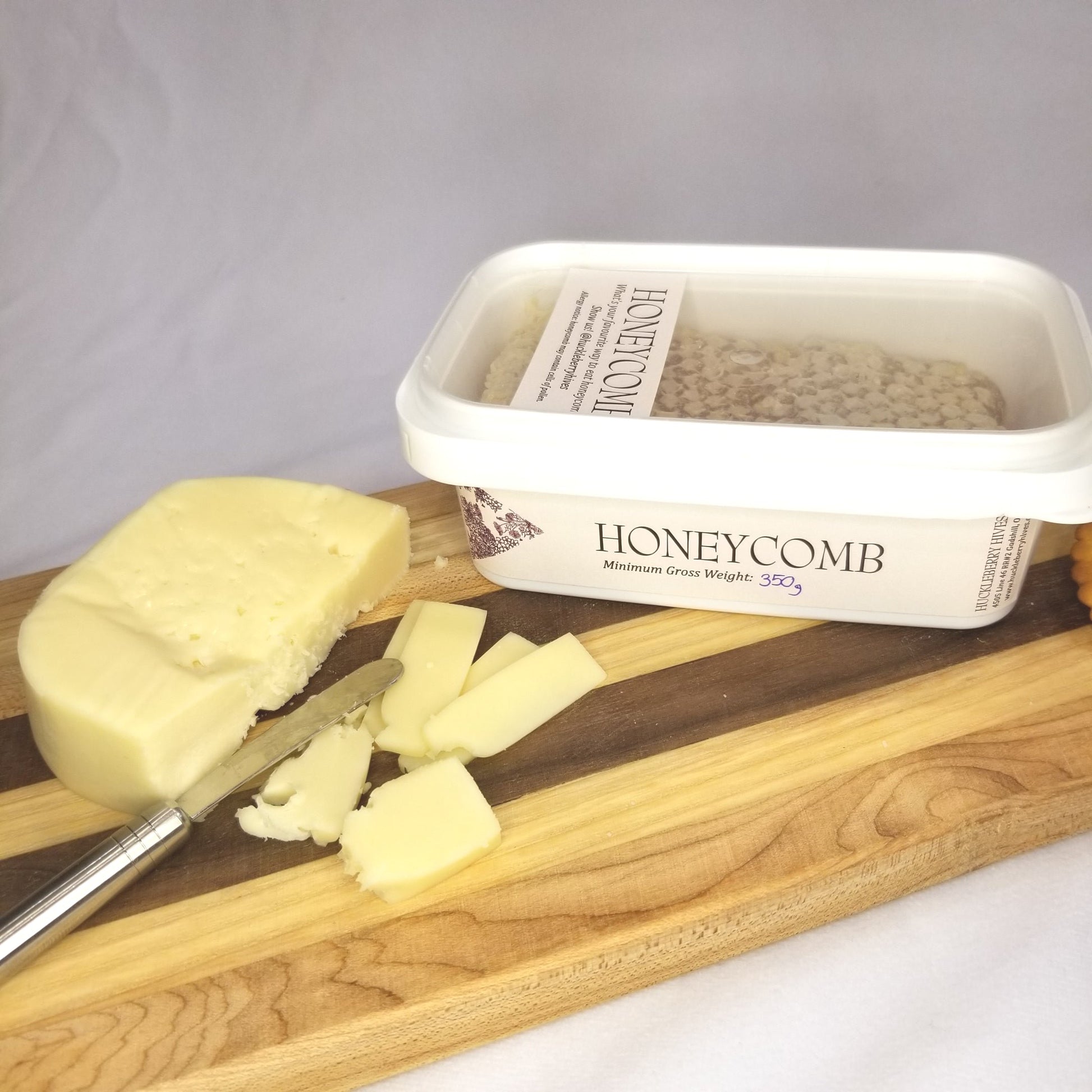 Packaged honeycomb sits beside cheese on a wooden charcuterie board.