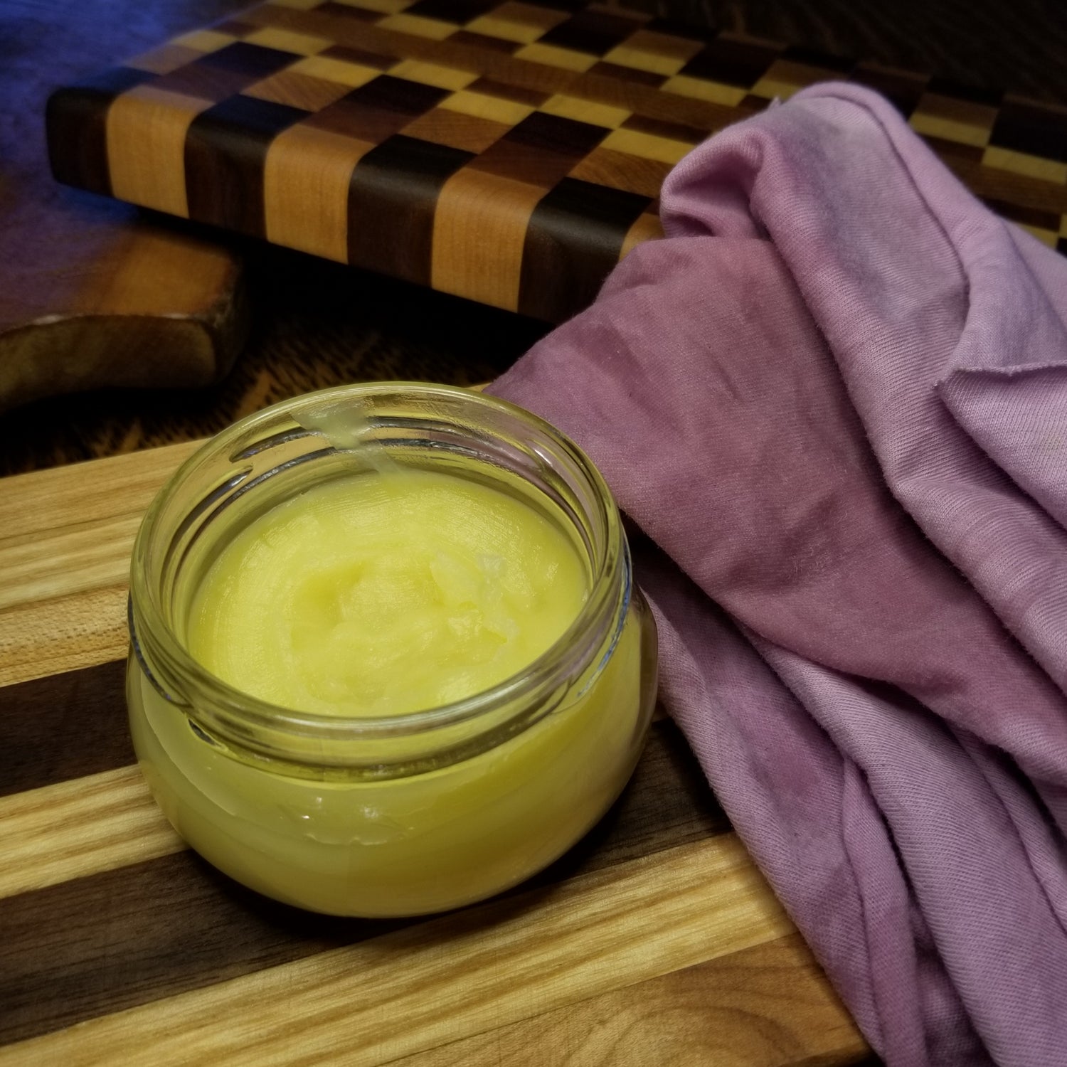 An open jar of board rub sits beside a soft buffing cloth for applying the butter to wooden cutting boards to condition the wood. 