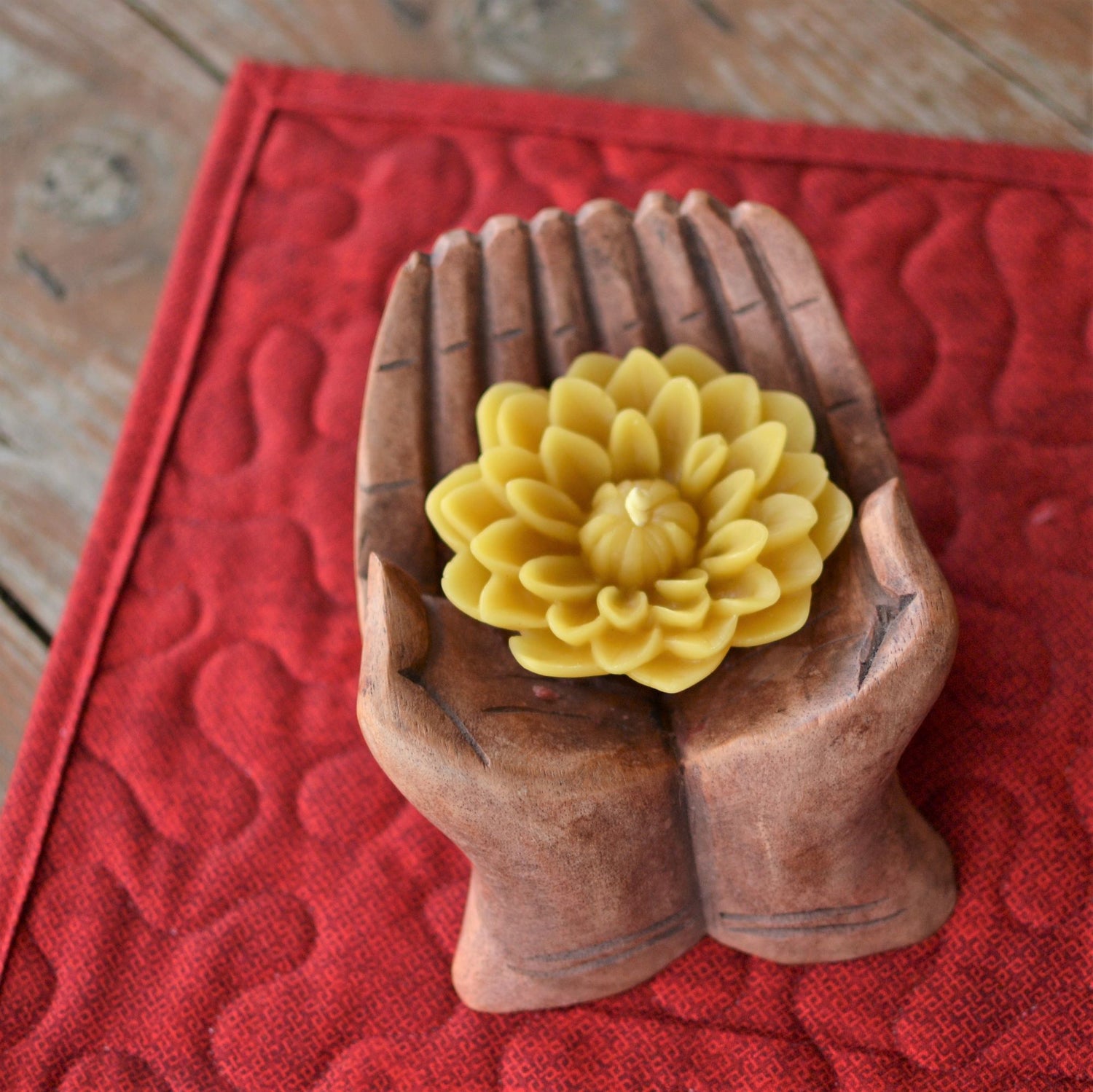 Yellow beeswax dahlia candle sitting in carved wooden giving hands
