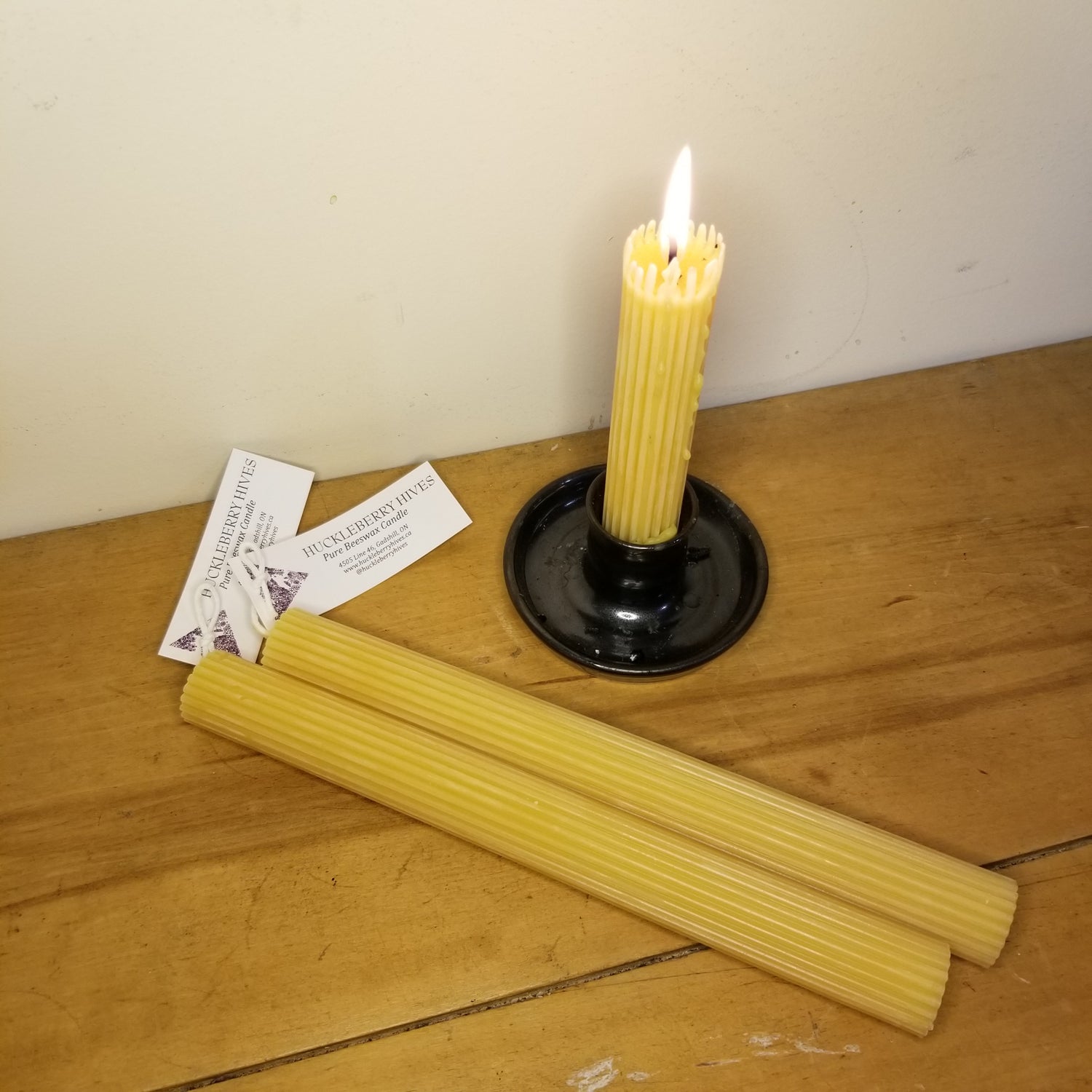 beeswax fluted taper candles lying beside a lit fluted taper in a black candle holder